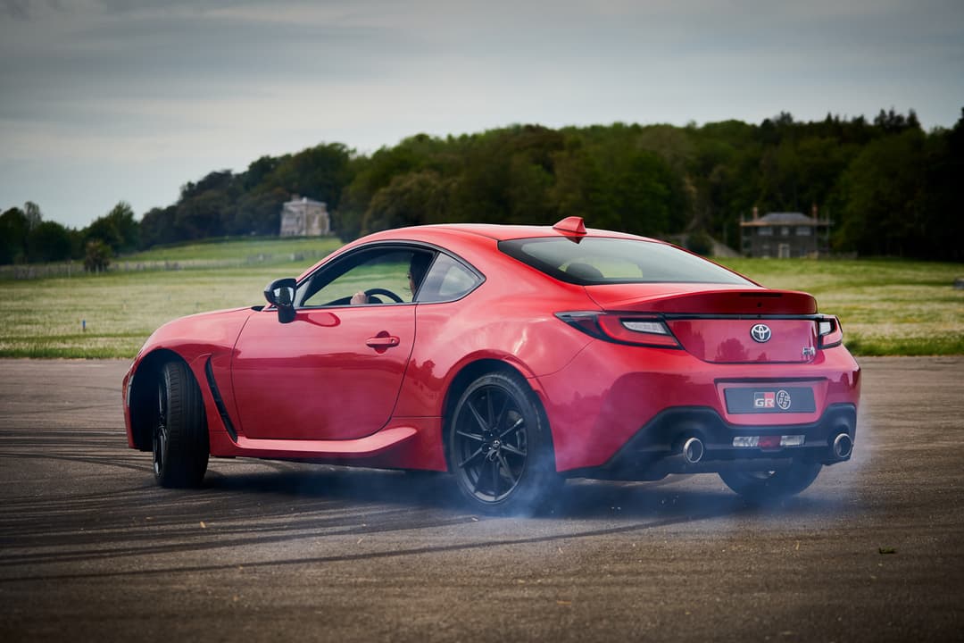 Toyota GR 86 rouge vif, coupé sportif deux portes, photographié de profil sur un circuit automobile dégagé