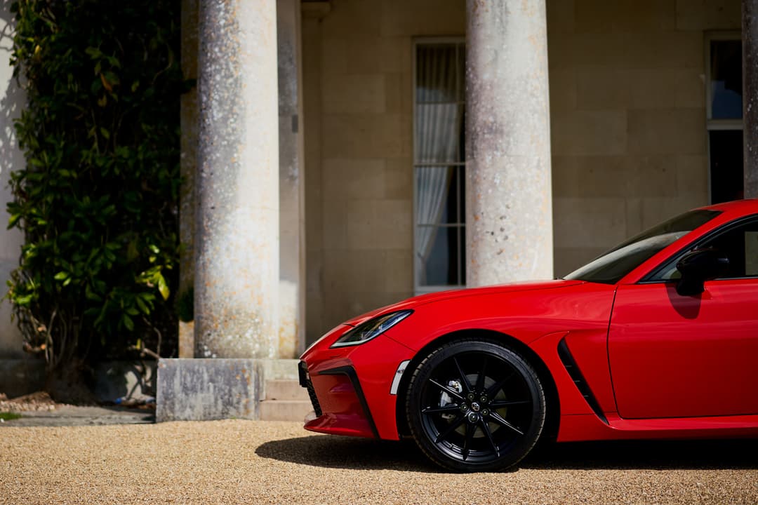 Toyota GR 86 rouge de profil, stationnée devant une façade classique avec colonnes blanches