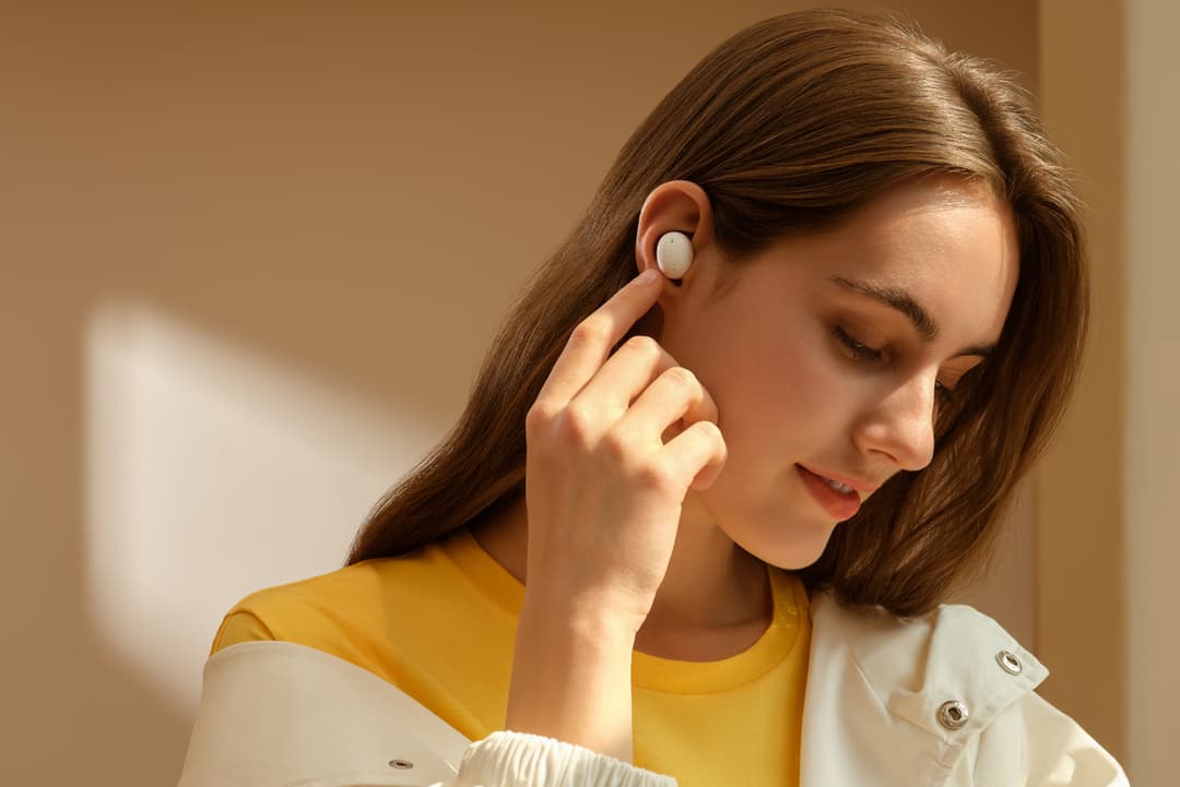 Écouteur OPPO Enco Buds blanc dans l'oreille d'une femme portant un t-shirt jaune
