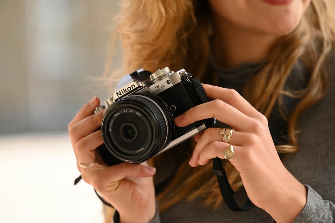 Nikon Z fc, appareil photo hybride compact au design épuré, tenu entre les mains d'une femme aux cheveux roux