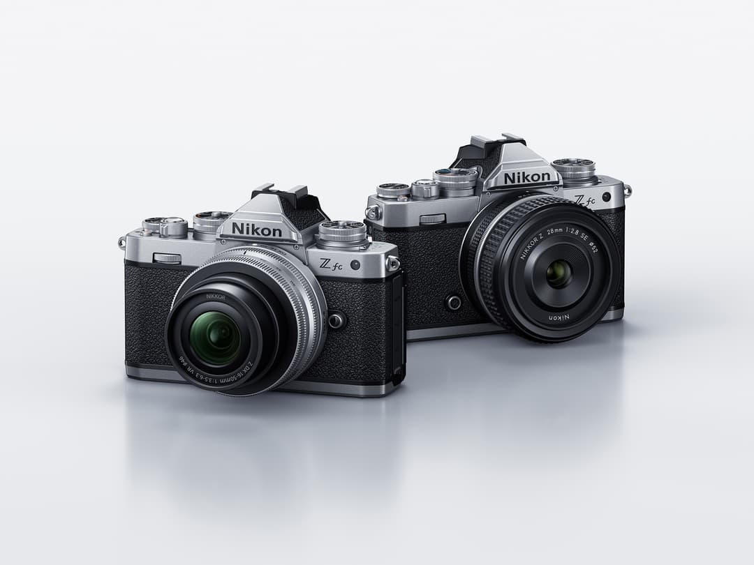 Deux appareils photo hybrides Nikon Z fc au design rétro, l'un argent avec objectif vert, l'autre noir, posés sur fond blanc