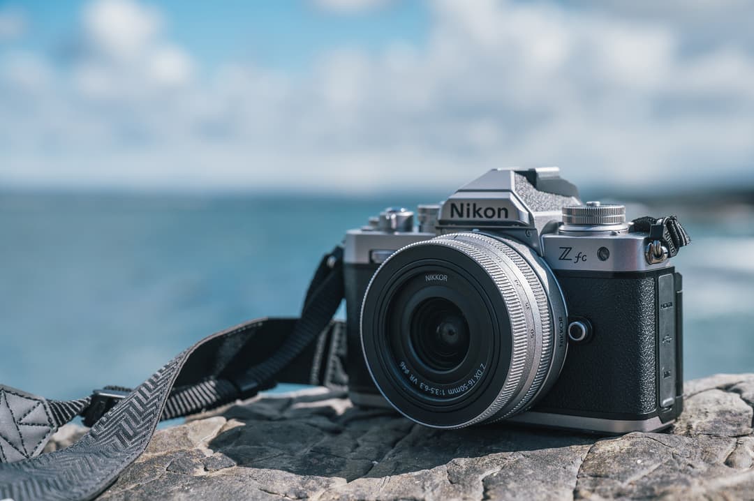 Nikon Z fc, appareil photo hybride noir et argenté au design rétro, posé sur une pierre face à la mer