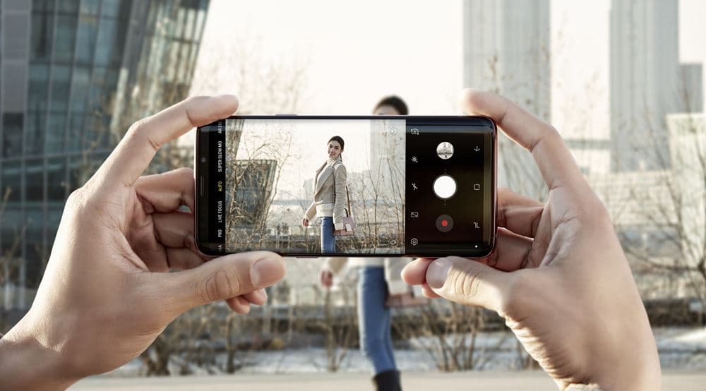 Mains tenant un Galaxy S9 affichant l'interface de l'appareil photo en mode portrait, une personne en arrière-plan