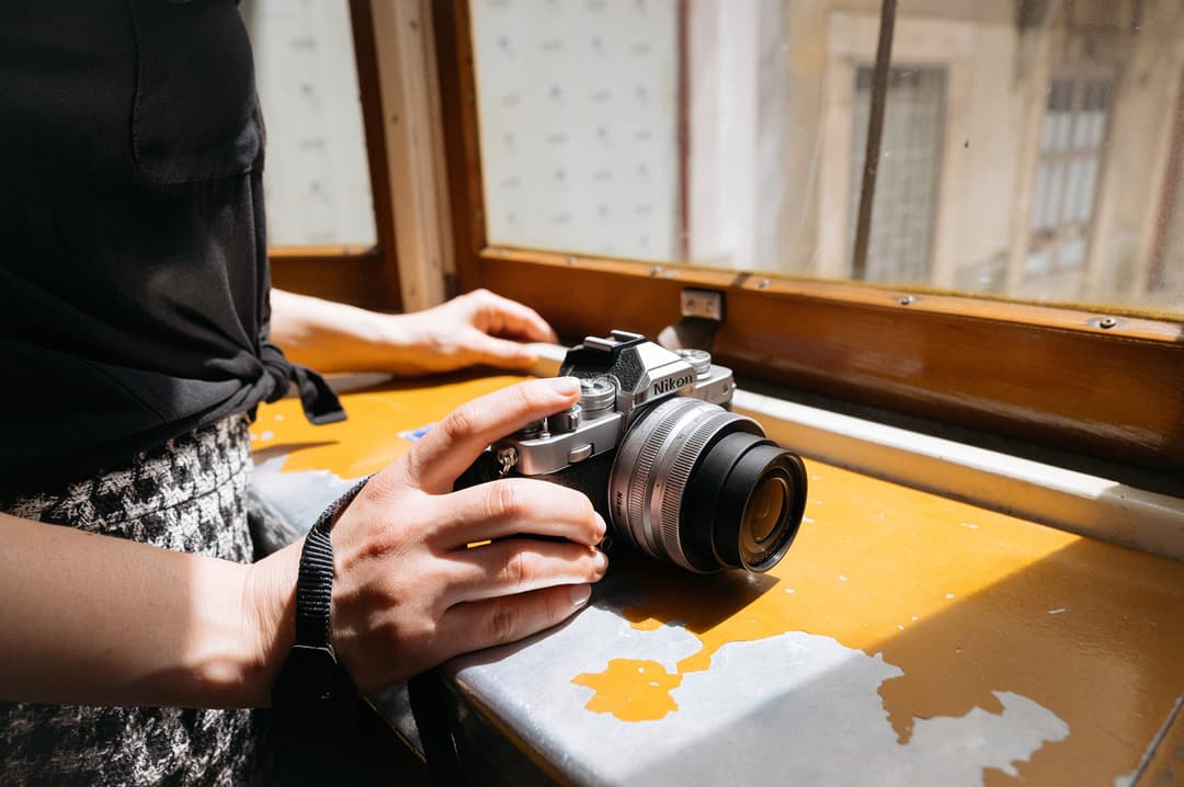 Appareil photo hybride Nikon Z fc tenu en main, posé sur une surface jaune près d'une fenêtre