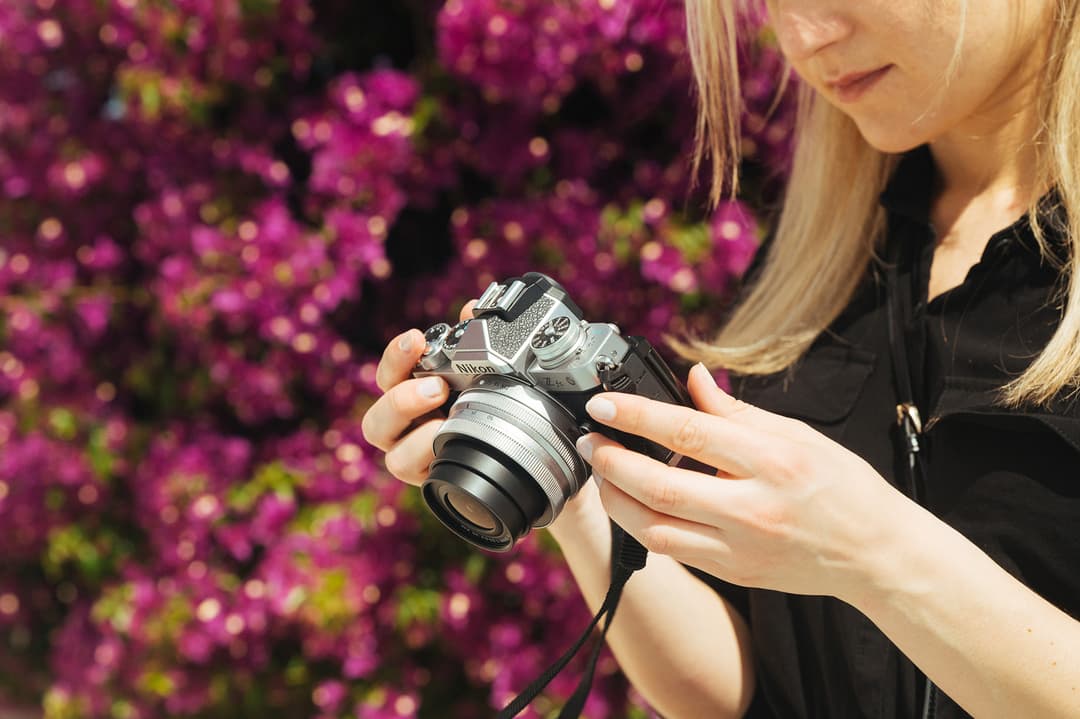 Femme tenant le Nikon Z fc, appareil photo hybride au design rétro, devant un fond de fleurs roses