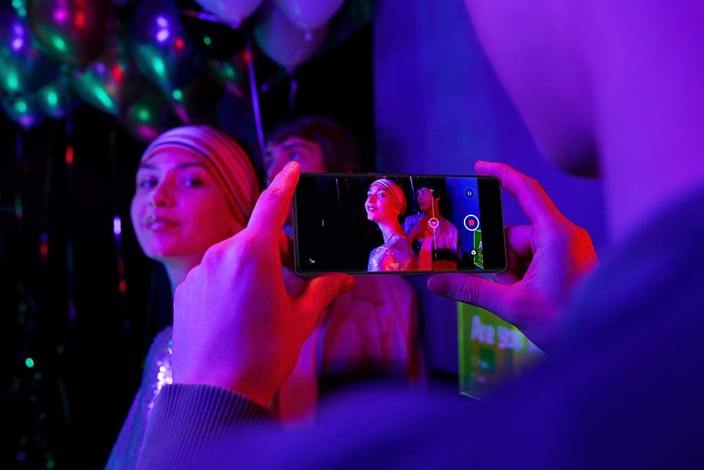 Personne filmant une scène nocturne colorée avec un smartphone OPPO Reno6 en mode Ultra Dark, éclairage néon rose et violet