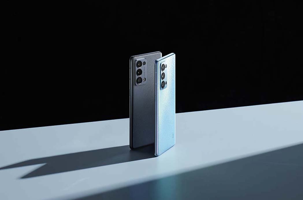 Deux smartphones OPPO Reno6, l'un noir et l'autre bleu clair, posés côte à côte sur une surface blanche sur fond noir