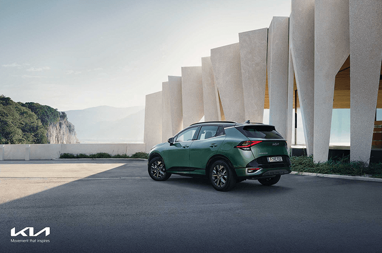 Kia Sportage vert face arrière gaucheprofil devant architecture moderne, montagnes en arrière-plan