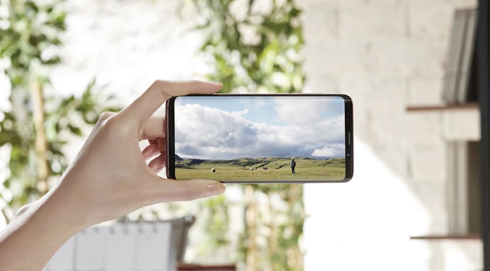 Samsung Galaxy S9 tenu en main affichant une vidéo de paysage avec ciel nuageux sur son écran Infinity Display