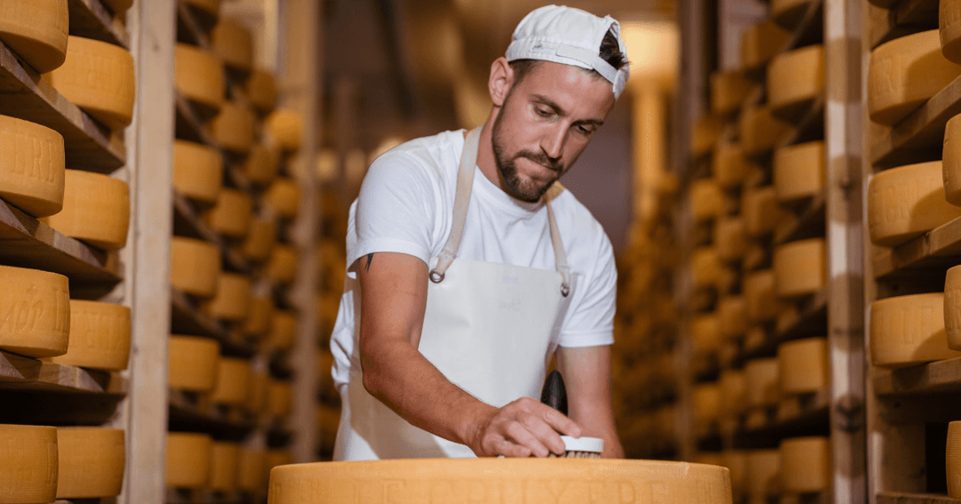 Fromager inspectant un meule de gruyère dans une cave d'affinage, entouré de fromages empilés sur des étagères