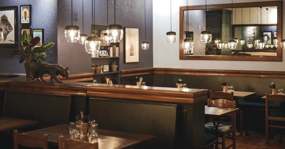 Intérieur du Boteco, bar avec comptoir en bois, luminaires suspendus, murs gris et noir, décoration moderne et épurée