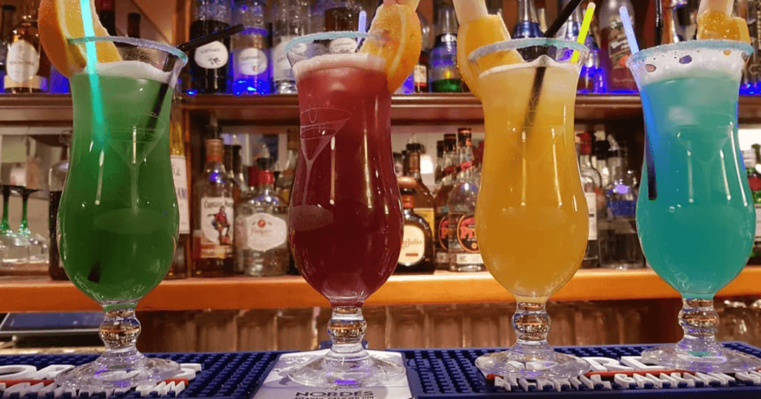 Quatre cocktails colorés alignés sur le comptoir du Radar de Poche à Genève, garnis d'agrumes et de glaçons, avec le bar éclairé en arrière-plan