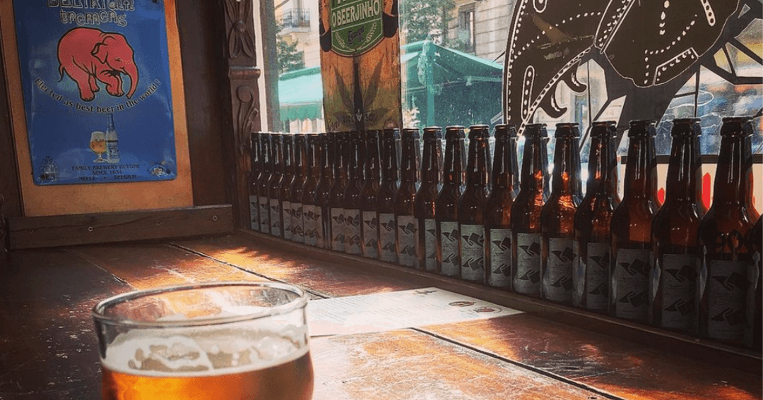 Verre de bière en premier plan avec rangée de bouteilles de bière brune et affiches de bar en arrière-plan