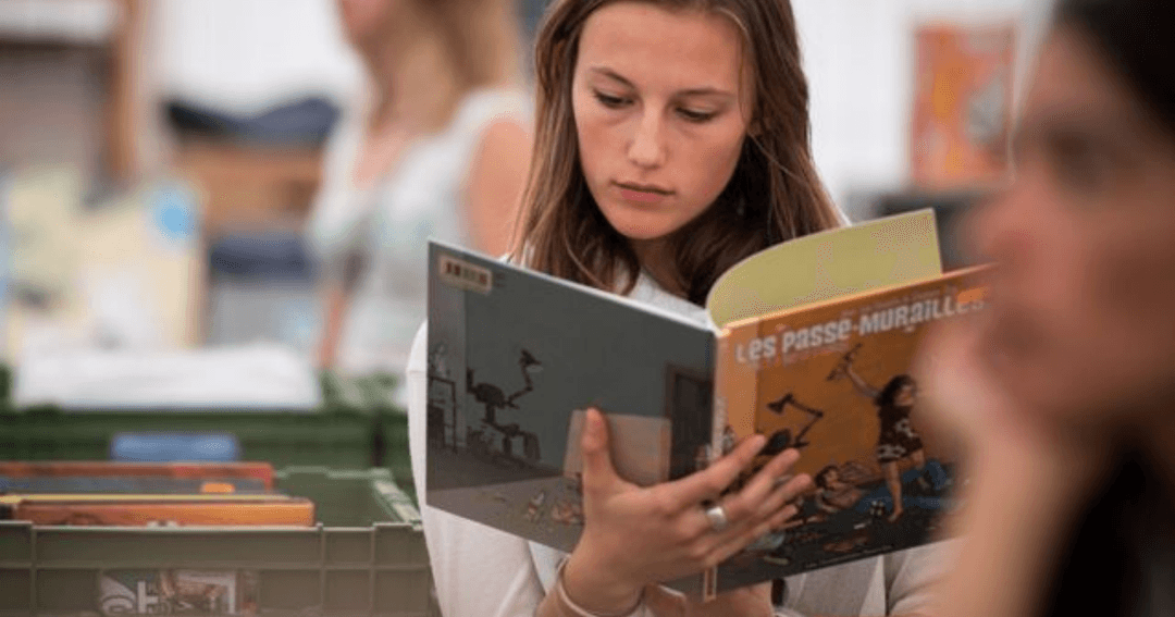 Une jeune femme consulte des livres sur un étal de la Fête livres & disques, avec d'autres ouvrages empilés sur la table