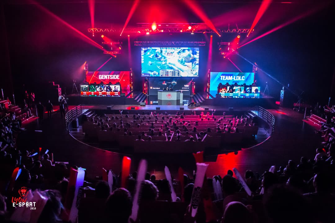 Scène de tournoi esport à Lyon avec écrans géants, éclairage rose et bleu, spectateurs dans la salle et équipes Gentside et Team-LDLC sur les côtés