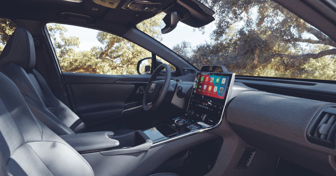 Intérieur du Toyota BZ4X avec sièges avant noirs, écran tactile coloré et vue dégagée sur la route