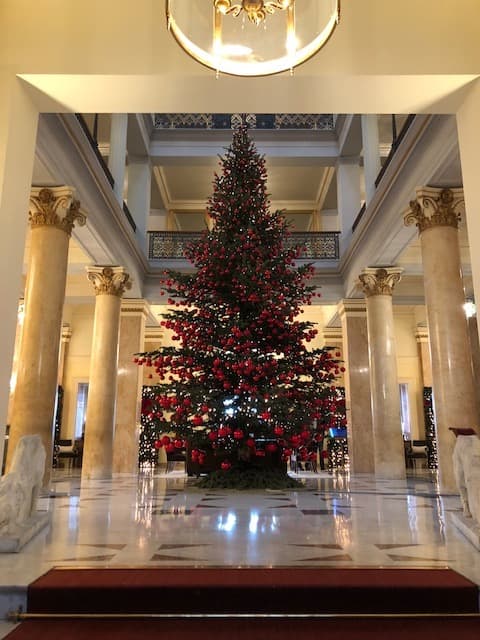 Grand sapin de Noël rouge et or dans le hall majestueux du Beau-Rivage Palace, entouré de colonnes dorées et de marbre blanc