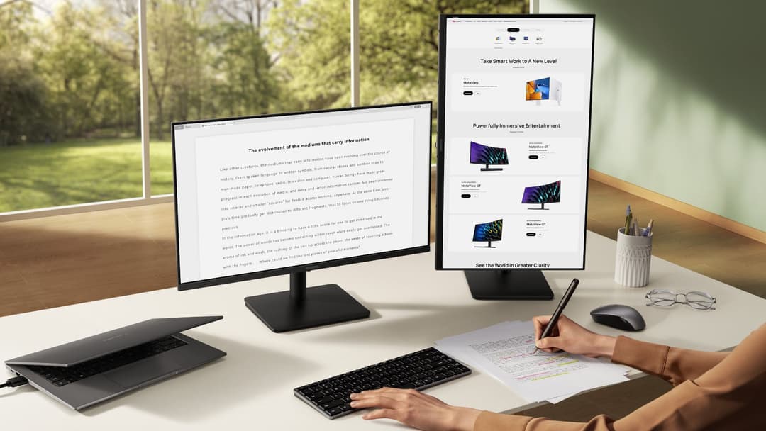Espace de travail avec deux écrans Huawei, clavier, souris et ordinateur portable, personne travaillant à un document avec vue sur un paysage boisé
