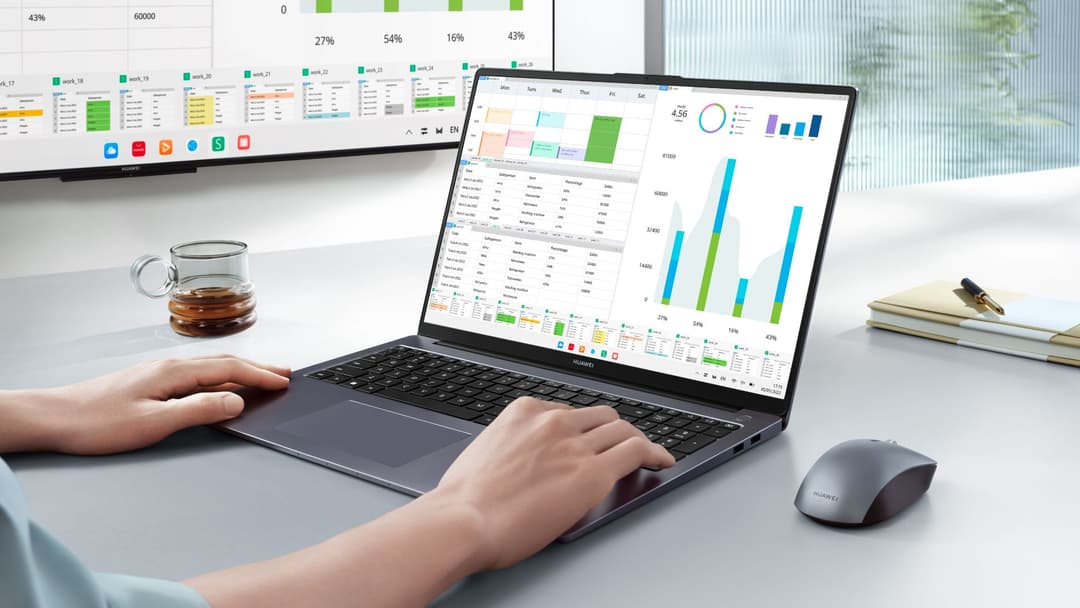 Environnement de travail avec laptop Huawei affichant des tableaux de bord analytiques, moniteur en arrière-plan, tasse de café et fournitures de bureau
