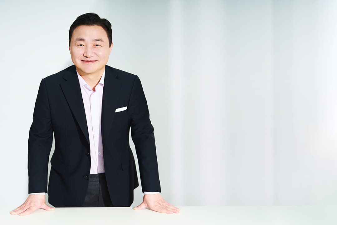 Dr Tae Moon Roh, président de la division MX de Samsung Electronics, en costume noir et chemise rose, souriant appuyé sur une table