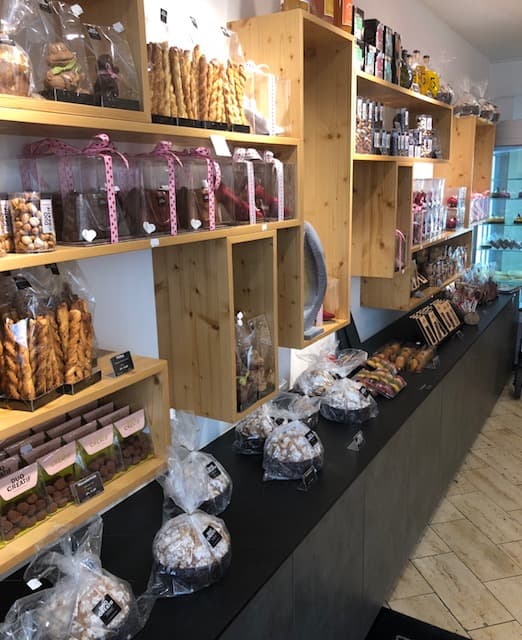 Boutique lumineuse avec étagères en bois affichant chocolats, pâtisseries, pains et pièces salées présentés en vitrines et sur comptoir noir