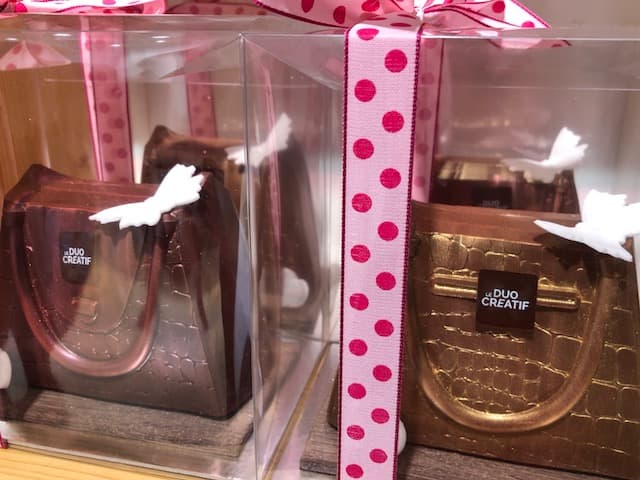 Sacs et escarpins en chocolat, présentés en vitrine avec ruban rose à pois rouges