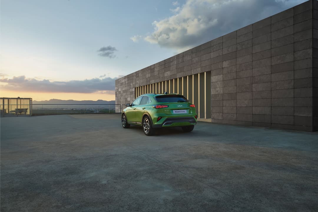 Kia XCeed vert citron de profil, stationnée devant un bâtiment moderne en brique, au coucher du soleil