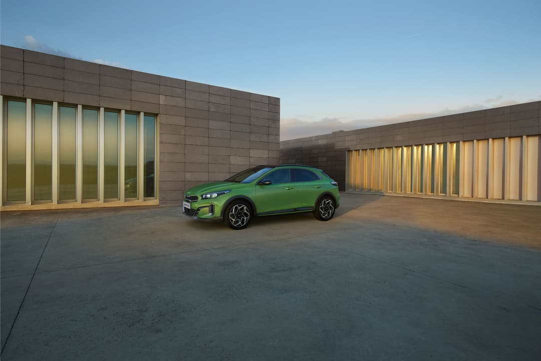 Kia XCeed vert citron stationnée dans une cour carrelée entourée de bâtiments en brique et verre, en fin d'après-midi