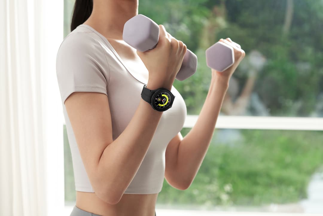 Femme portant une Galaxy Watch5 au poignet, faisant des exercices avec des haltères gris