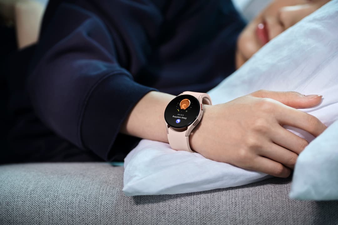 Galaxy Watch5 rose au poignet d'une personne allongée dans un lit, écran affichant l'interface de sommeil