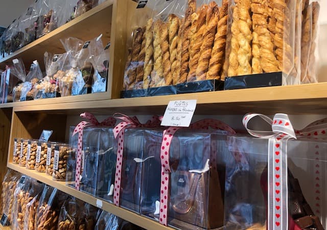 Vitrines en bois d'une boutique de pâtisserie et chocolaterie avec pains tressés, chocolats et pièces salées présentés en sachets transparents