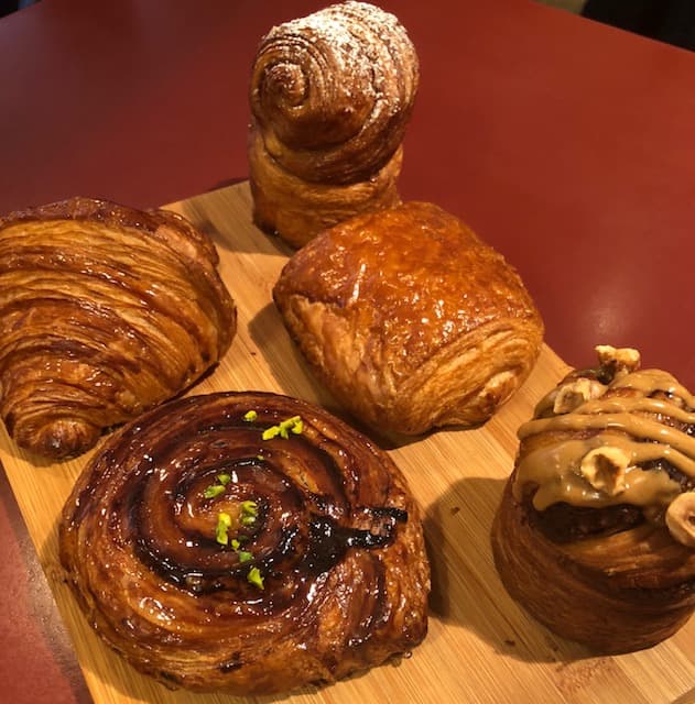 Assortiment de viennoiseries du Duo Créatif : croissant feuilleté, brioche pralinée avec glaçage brillant, pain au chocolat et brioche aux noix sur planche en bois