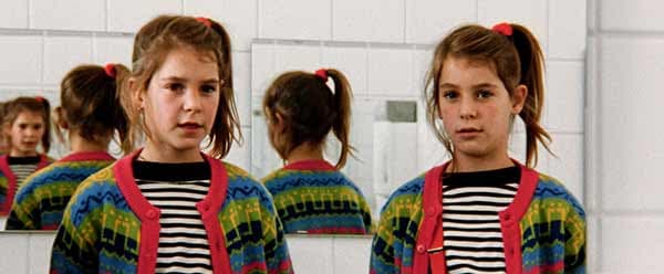 Deux enfants portant un cardigan coloré rouge et bleu avec rayures noires et blanches, photographiés de face devant un mur blanc