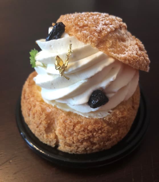 Chou à la crème garni de crème fouettée, confit de cassis noir et sucre perlé, sur assiette noire