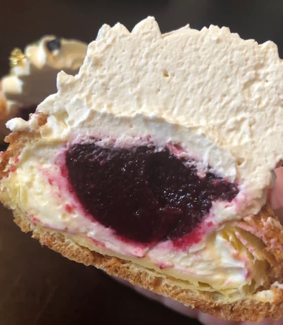 Chou à la crème généreuse, garni d'une couche de confit cassis bordeaux et couronné de crème pâtissière blanche