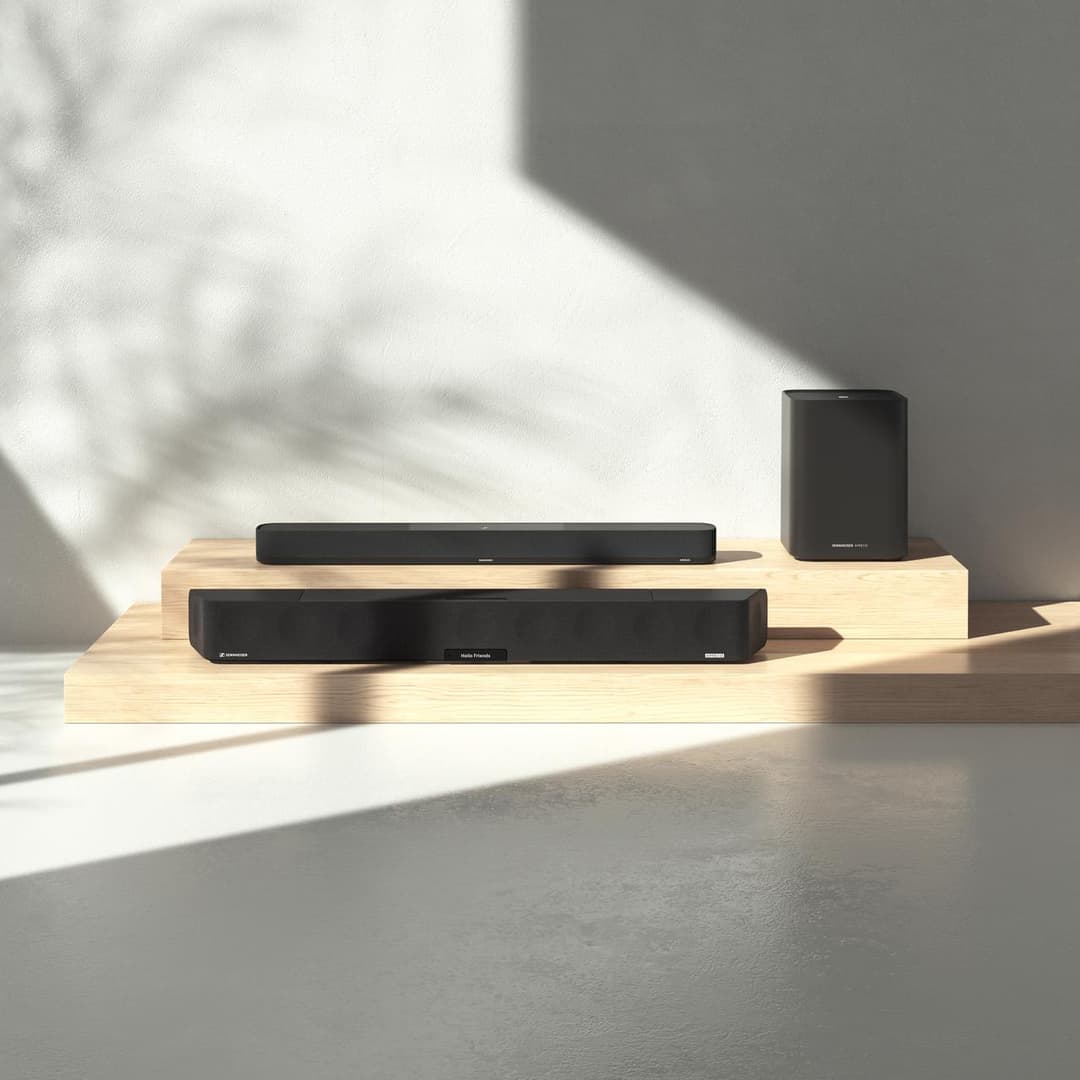 Barres de son Sennheiser Ambeo noires et caisson de basses sur socles en bois clair, dans un intérieur lumineux