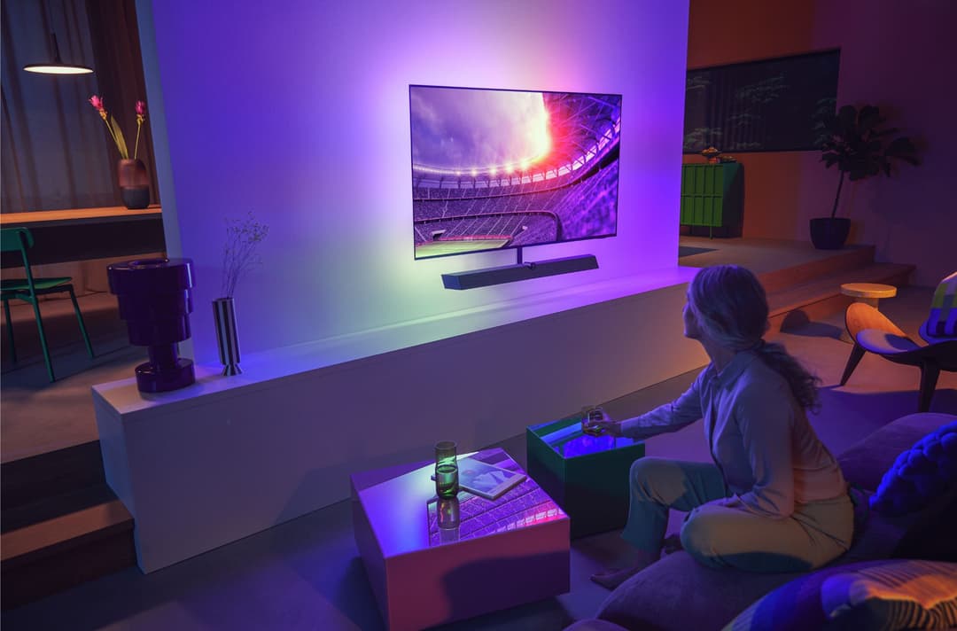 Téléviseur Philips Ambilight affichant un stade de football, ses LED changeant l'éclairage du salon en violet et rose