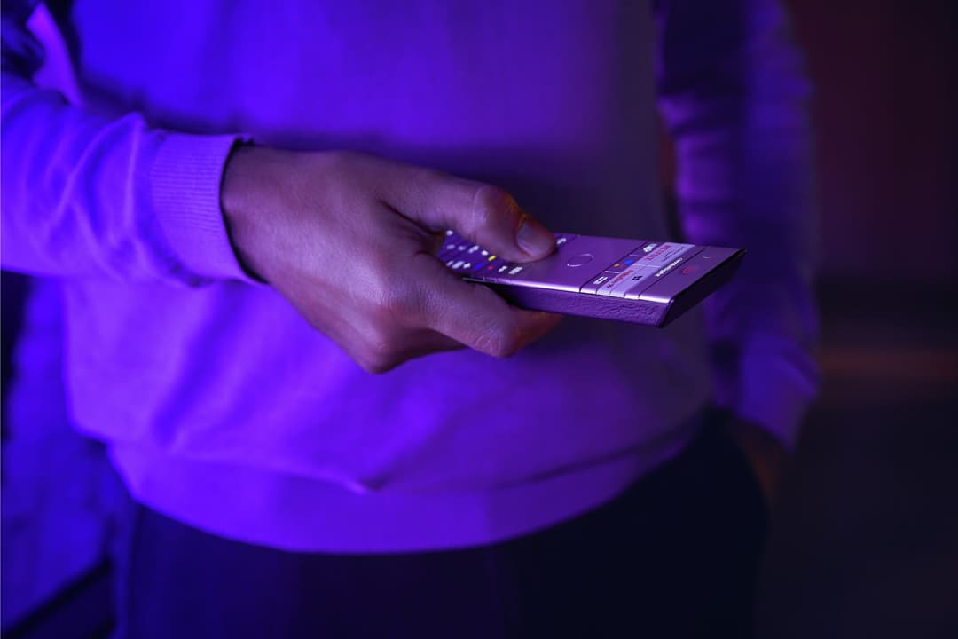 Télécommande Philips rétroéclairée en métal argenté avec dos en cuir, tenue dans une main sous lumière violette