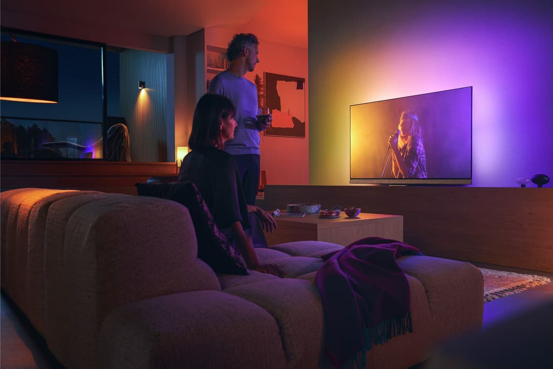 TV Philips Ambilight affichant une chanteuse, avec éclairage ambiant synchronisé en orange et violet dans un salon