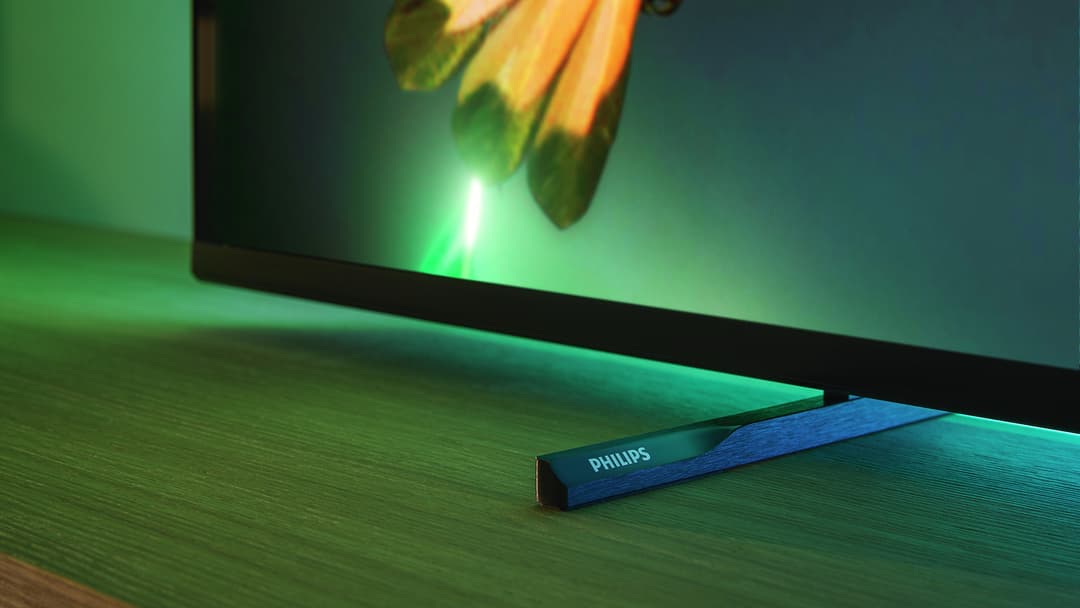 Barre sonore Philips bleue posée devant un téléviseur Ambilight affichant une image verte, avec éclairage Ambilight vert vif