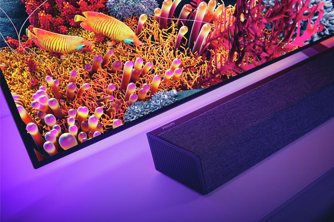 Téléviseur Philips avec contenu récif corallien coloré, illuminé par Ambilight rose et violet, accompagné d'une barre de son Bowers & Wilkins