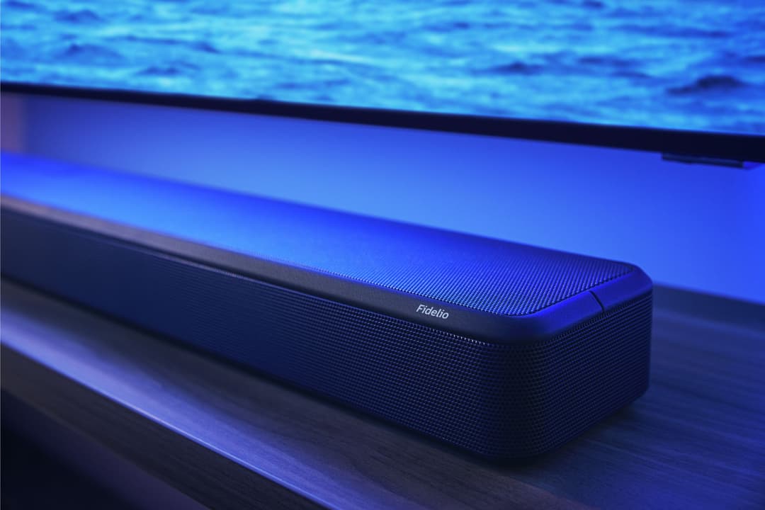 Barre de son Philips Fidelio noire posée sous un écran de télévision affichant une image d'eau bleue