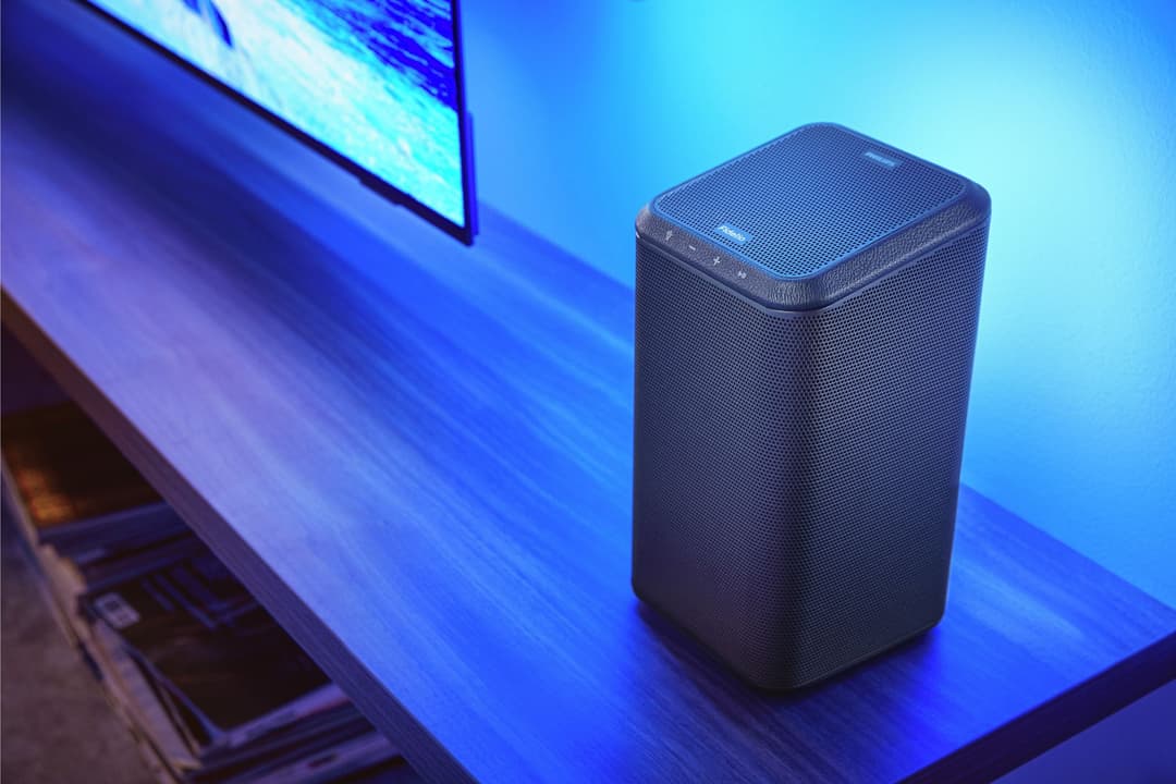 Enceinte Fidelio FS1 noire sur meuble bleu, devant écran de télévision, en ambiance lumineuse bleue