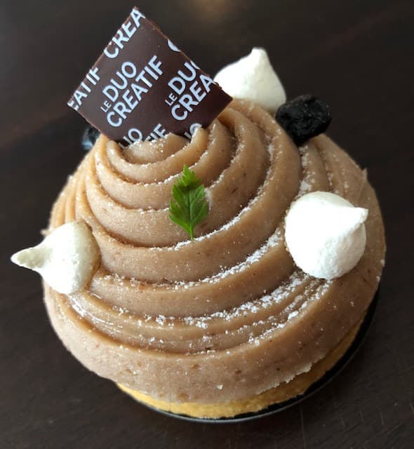 Pâtisserie en spirale à base de crème marron, saupoudrée de sucre glace, décorée de meringues blanches et d'une feuille de menthe verte