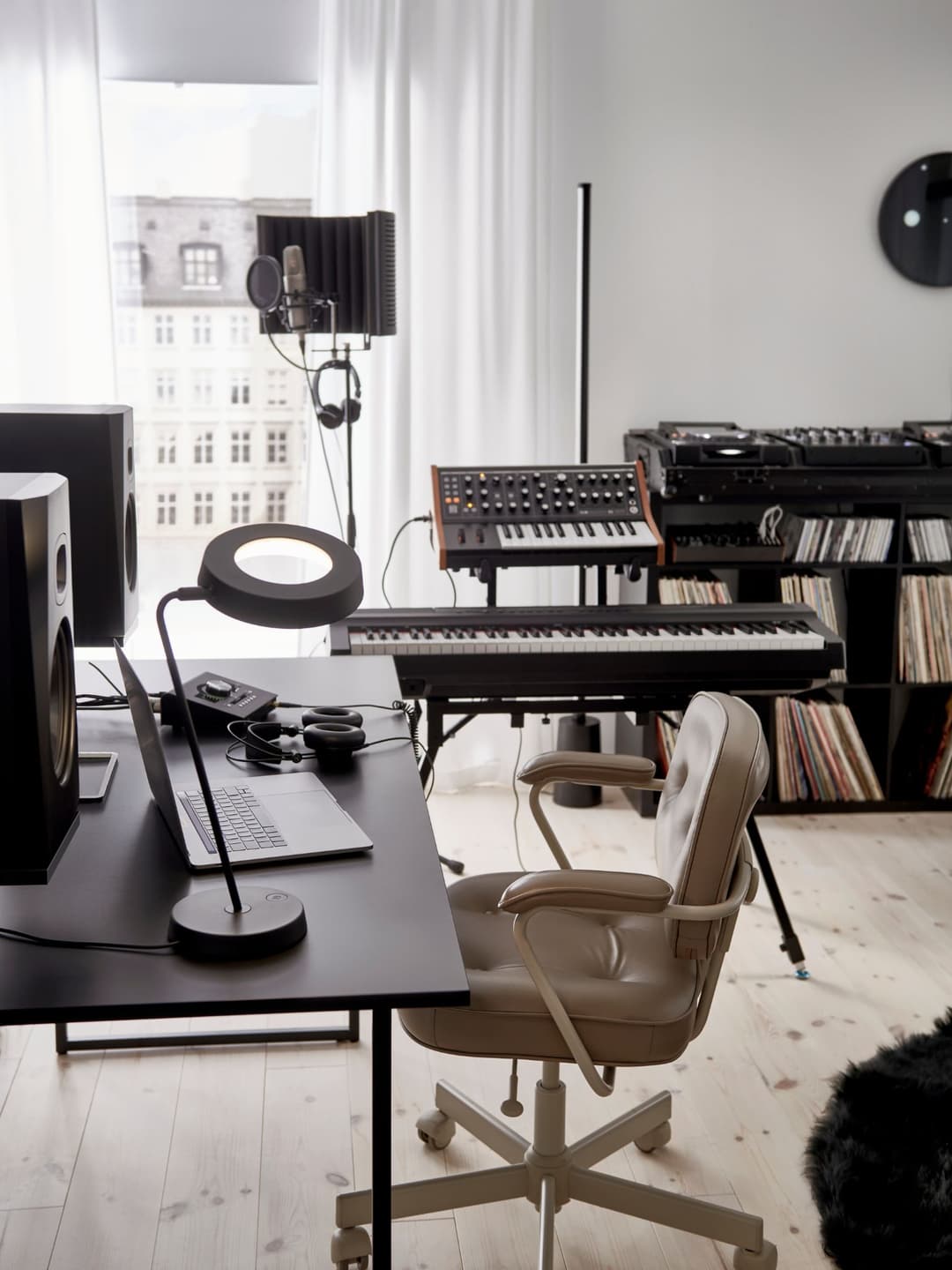 Studio de musique aménagé avec meubles IKEA : table noire, chaise beige, claviers électroniques, microphone, casque audio et rangements pour vinyles