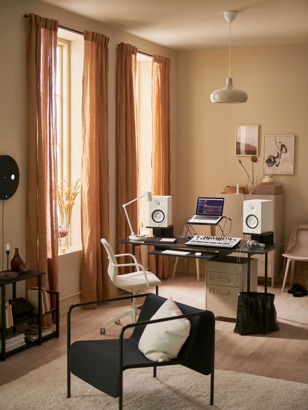 Studio de création IKEA OBEGRÄNSAD avec bureau noir, enceintes blanches, laptop, clavier, chaise blanche, fauteuil noir et rideaux ocre aux fenêtres