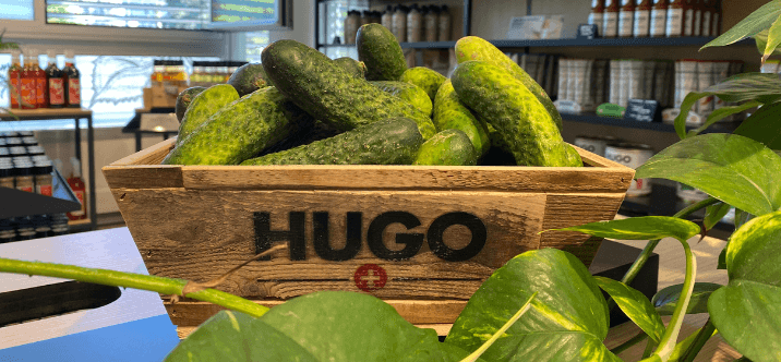 Caisse en bois HUGO remplie de cornichons verts disposée dans un magasin Reitzel