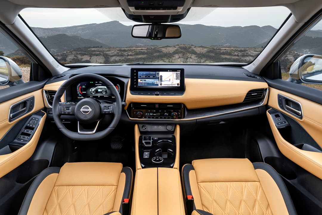 Habitacle du Nissan X-Trail avec sièges avant en cuir beige, console centrale avec rangements et écran tactile, vue panoramique de montagne