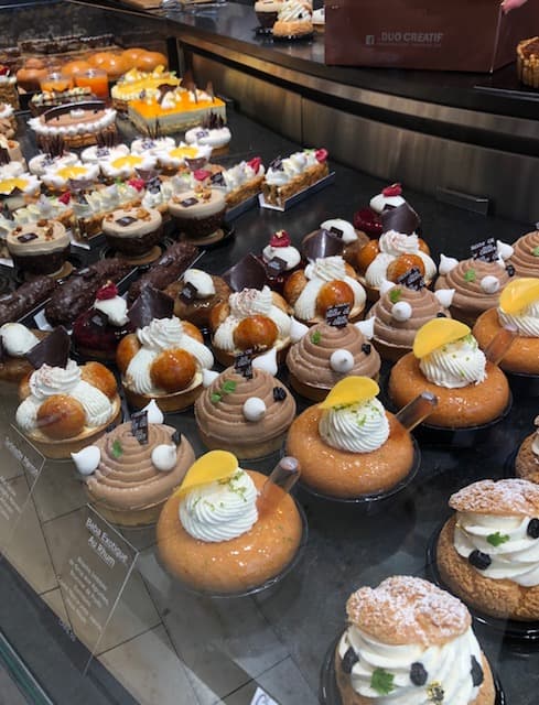 Vitrine de pâtisserie avec choux à la crème garnis de glaçage blanc et fruits, religieuses au chocolat et desserts variés