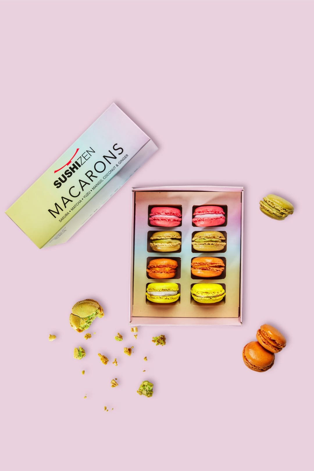 Boîte de macarons SushiZen aux saveurs nippones avec huit pièces colorées rose, jaune, doré et orange sur fond rose
